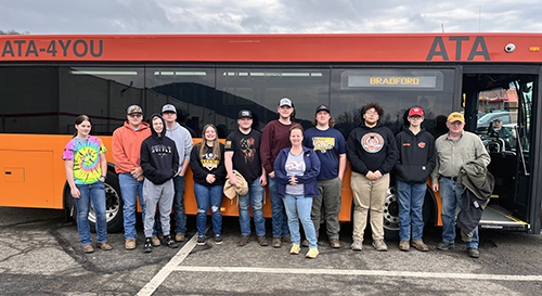 Group of students and adults in front of tour bus