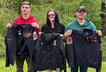 Three students outside holding up jackets